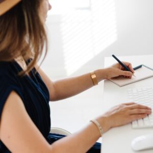 A woman sitting at a desk writing on a notepad.