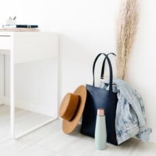 A blue handbag sitting on the floor with a denim jacket, a metal water bottle, and hat beside it.