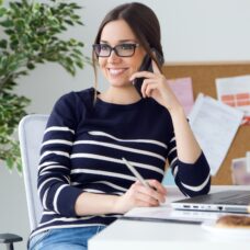 A smiling woman sitting at a desk talking on a cell phone.