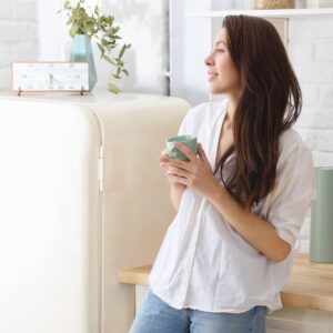 A woman wearing jeans and a white top standing in a kitchen holding a light green coffee mug.