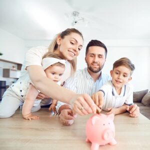 A smiling family putting a coin into a pink piggy bank.